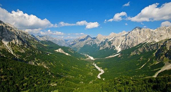 Panoramic view of Valbona Valley with green alpine mountains and clear skies in northern Albania