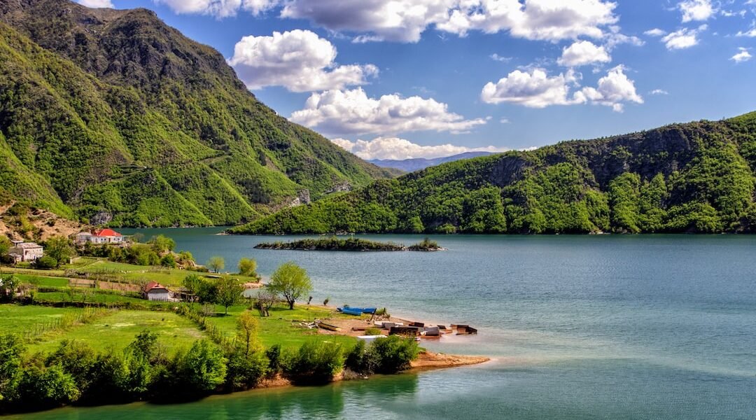 http://Lakeside%20view%20of%20Voskopoja%20with%20mountains%20in%20the%20background%20under%20a%20bright%20blue%20sky.